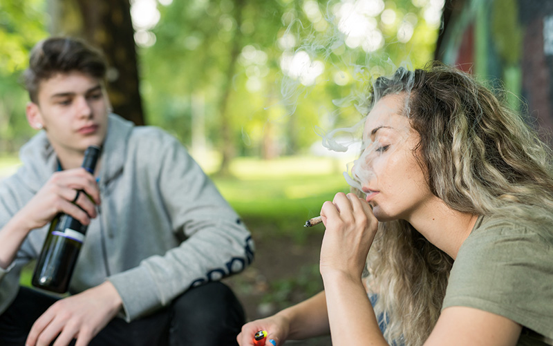 Two high school teens drinking and smoking marijuana in a park
