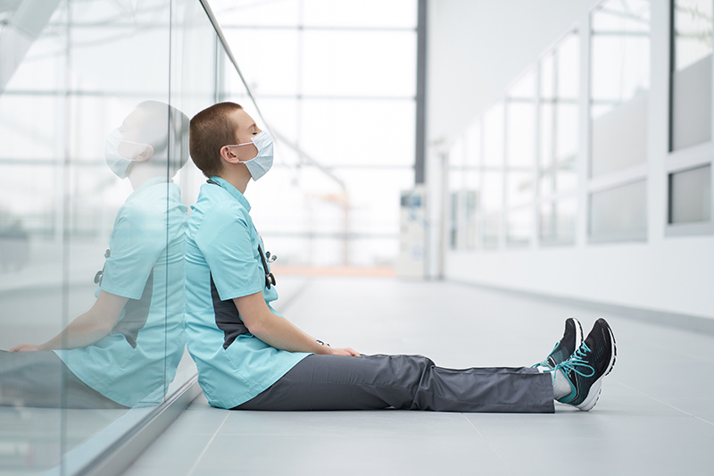 Burnout concept. Exhausted doctor sitting on a floor in corridor of clinic with closed eyes